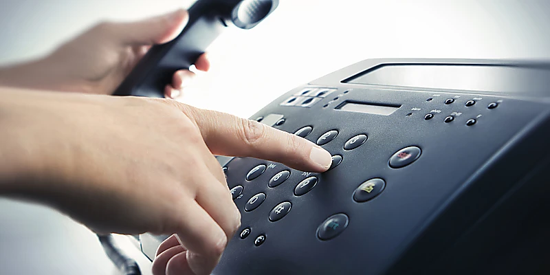 Hand beim Wählen einer Telefonnummer an einem Bürotelefon.