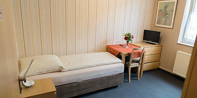 Einzelzimmer mit Einzelbett, Sitzecke und Fernseher.